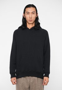 Felpa nera con cappuccio, tasca a marsupio, polsini a costine e vestibilità comoda. Tessuto morbido, senza motivi o dettagli visibili.