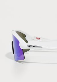 Occhiali da sole sportivi bianchi con design avvolgente, lenti gradienti viola e verde, dettagli metallici e un logo del marchio ben visibile sul lato.