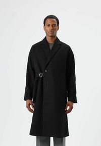 Schwarzer Wollmantel mit einer einzelnen Knopfleiste, breiten Revers und abnehmbarem Gürtel. Verfügt über eine lockere Passform und ein mittellanges Design.