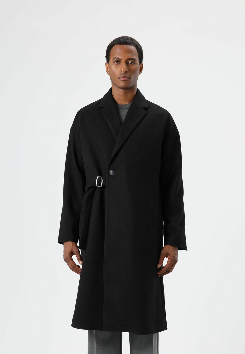 Schwarzer Wollmantel mit einer einzelnen Knopfleiste, breiten Revers und abnehmbarem Gürtel. Verfügt über eine lockere Passform und ein mittellanges Design.