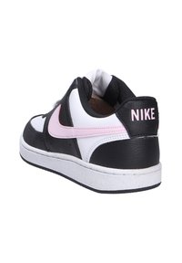 Zapatilla en blanco y negro con acentos en rosa, textura de cuero, punta redondeada, suela plana de goma y marca Nike visible en el talón.