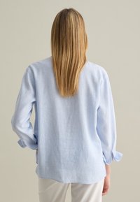 Helles blaues, langärmliges Hemd mit Knopfleiste und Kragen, Rückenfalte und gekrempelten Ärmeln. Hergestellt aus einem strukturierten Stoff mit dezenten Streifen.