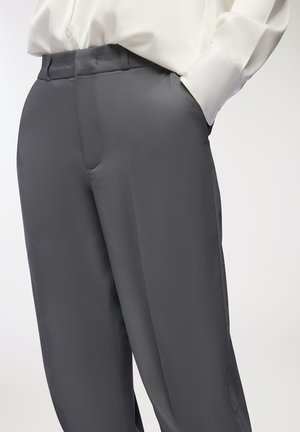 Pantaloni in satin grigio con una texture liscia, caratterizzati da una vestibilità sartoriale e tasche laterali, abbinati a una camicia bianca con bottoni.