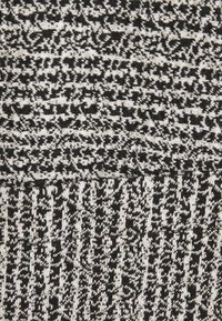 Svart och vit stickad tyg som har ett texturerat mönster. Tyget har varierande tjocklek och designelement, vilket skapar visuell intresse.