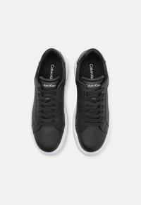 Black leather sneakers with white rubber soles, featuring a textured side panel, contrasting laces, and a subtle logo on the tongue.