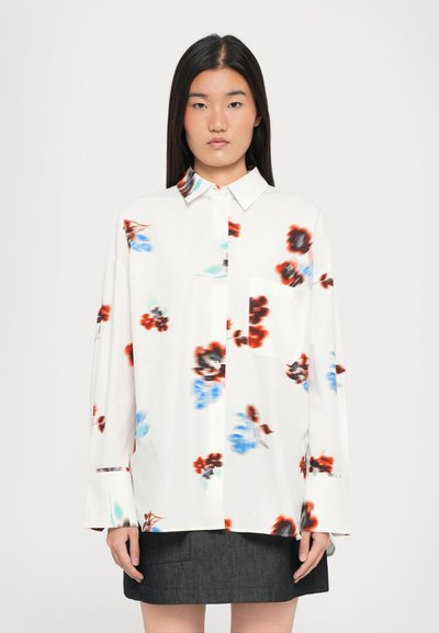 Witte blouse met lange mouwen en bloemenprint in rood, blauw en zwart. Voorzien van een knoopsluiting aan de voorkant, een kraag en een enkele borstzak.