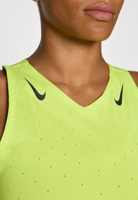 Top sportivo senza maniche verde neon con scollatura a V, caratterizzato da dettagli neri e piccole perforazioni per la ventilazione, logo sulla spalla sinistra.