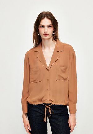 Brown, long-sleeve blouse in lightweight fabric, featuring a button front, two chest pockets, and adjustable drawstring at the hem.