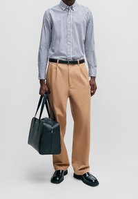 Randig skjorta med knappar, beige byxor, svarta läderskor och en svart läderväska. Skjortan har långa ärmar och krage; byxorna är löst sittande.