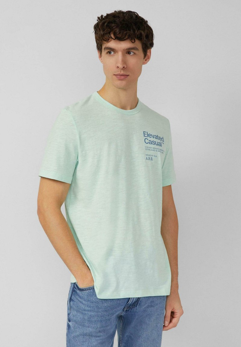 Licht muntgroen T-shirt met korte mouwen, gemaakt van zachte stof, met een blauw geprint logo op de borst, gecombineerd met blauwe spijkerbroek.