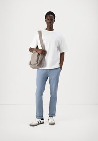 Tricou alb din bumbac, pantaloni bleu deschis, geantă de umăr gri cu fermoar și adidași albi cu dungi negre; stând pe un fundal simplu.