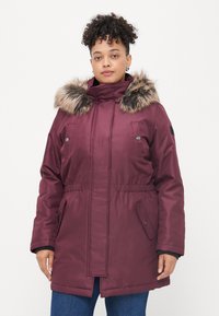 Parka isolada bordeaux com capuz de pelo sintético, cintura elástica, dois bolsos frontais e fecho éclair à frente. Design de tecido elegante e texturado.