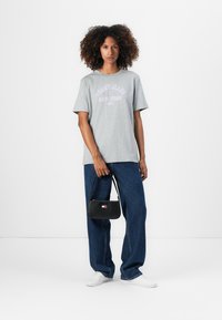 T-shirt en coton gris avec l'inscription "TOMMY JEANS NEW YORK", coupe décontractée, associé à un jean baggy bleu et un petit sac à main noir. Des baskets blanches complètent le look.