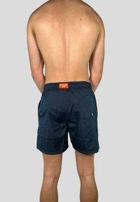 Pantaloni da bagno blu navy realizzati in tessuto leggero, con un elastico in vita e un’etichetta arancione, oltre a una tasca sul retro.