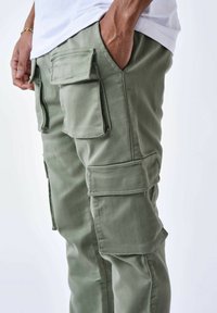 Pantalones cargo de algodón en verde oliva, con múltiples bolsillos laterales, un diseño ajustado y detalles de costura visibles. Textura suave.