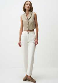 Beige ärmelloser, kurzer Blazer mit drei Knöpfen, kombiniert mit weißen, hoch taillierten Hosen, beide mit klaren Linien und minimalistischem Design.