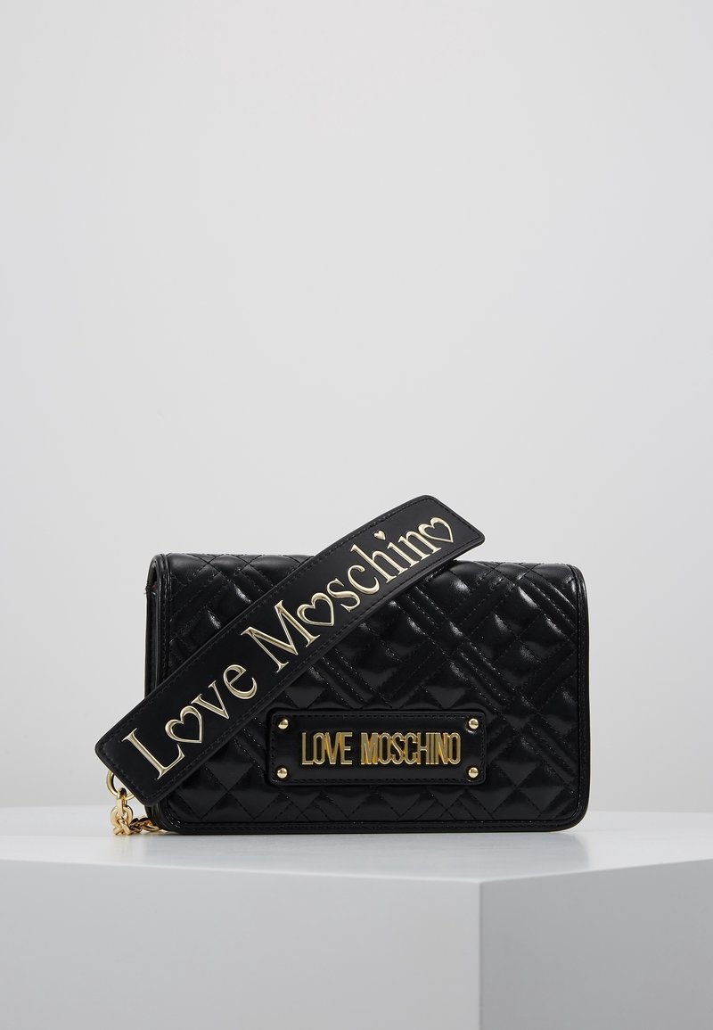 Černá prošívaná kabelka se zlatou nášivkou s nápisem "LOVE MOSCHINO" a ozdobným popruhem, který je rovněž embosovaný s názvem značky.