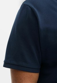 Dunkelblaues Poloshirt aus strukturiertem Stoff, mit kurzen Ärmeln und klassischem Stehkragen. Mit sichtbaren Nähten und glatter Oberfläche.