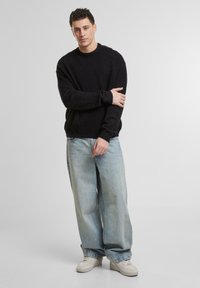 Maglione nero in maglia con scollatura rotonda, abbinato a jeans a gamba larga blu chiaro e sneakers bianche. Design semplice, vestibilità rilassata.