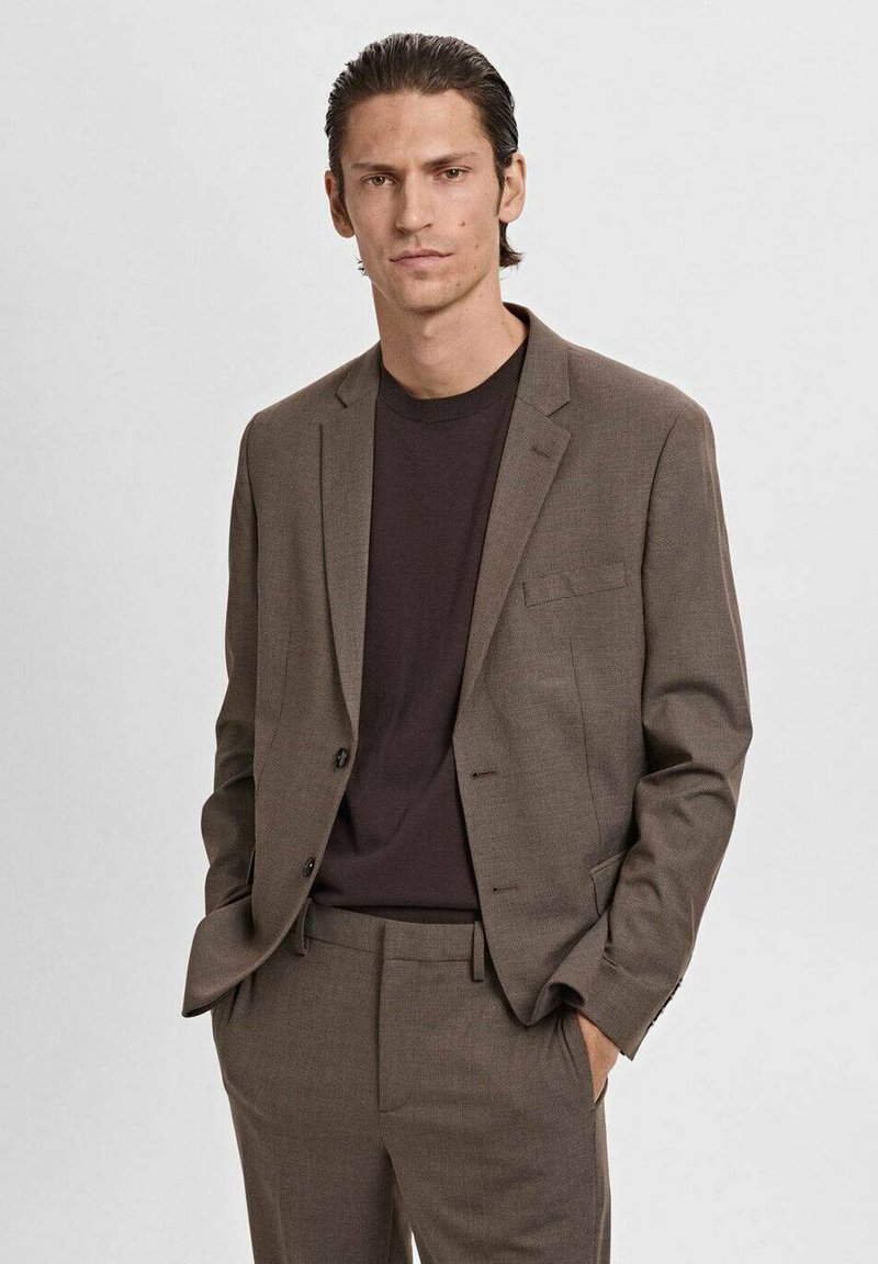 Bruine blazer met notch-lapels, een enkele zak en twee knopen, gecombineerd met een donker T-shirt. Op maat gemaakt met een soepele textuur.