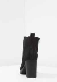 Botte cheville noire avec une finition en daim, talon bloc haut et fermeture éclair sur le côté. Comprend des panneaux élastiques pour un enfilage facile et une silhouette lisse et fuselée.