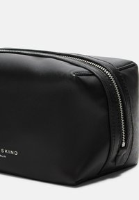 Porta trucchi in pelle nera con forma rettangolare, dotato di chiusura con zip argentata e logo del brand impresso sul fronte. Texture liscia.