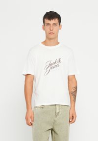 Fehér pamut póló, elöl egy barna, "Jack & Jones" felirattal. Rövid ujjú, kerek nyakú és laza szabású.