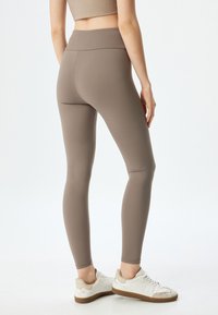 Bruine leggings met een hoge tailleband, naadloos ontwerp, gladde textuur en enkel-lange pasvorm, gecombineerd met witte sneakers.