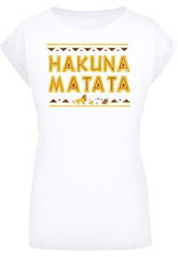 Valkoinen lyhythihainen t-paita, jossa on "HAKUNA MATATA" keltaisella, eläinkuvituksia ja geometrisia kuvioita maanläheisissä sävyissä.
