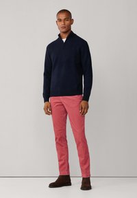 Marineblaues Zip-Kragen-Pullover, rosa Chinos und braune Knöchelschuhe. Der Pullover hat einen gerippten Saum, die Chinos sind slim-fit und die Schuhe bestehen aus glattem Leder.