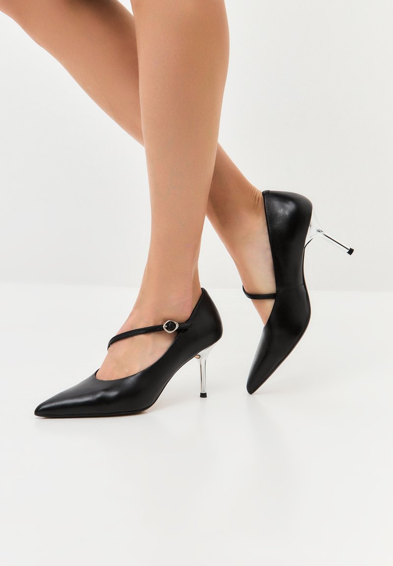 Tacchi alti in pelle nera con punta affusolata, caratterizzati da una fascia decorativa sopra l'arco del piede e un tacco a stiletto metallico lucido.