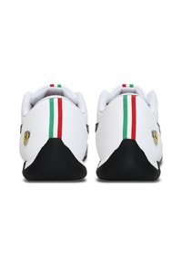 Chaussures de sport blanches avec une semelle noire, comportant des rayures rouges et vertes sur les talons et un logo Ferrari jaune sur le côté.