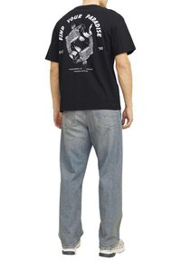 T-shirt in cotone nero con una grafica di pesci e testo sul retro. Abbinato a jeans in denim chiari e larghi.
