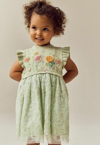 Lichtgroene jurk met een gebreid lijfje met bloemenborduursels en gerimpelde mouwen, en een elegante rok van geborduurde kant.