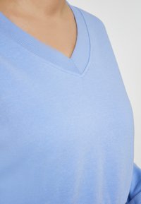 Maglione in cotone azzurro chiaro con scollatura a V, texture morbida e bordo ribattuto attorno al colletto. Primo piano che mostra la liscezza del tessuto.