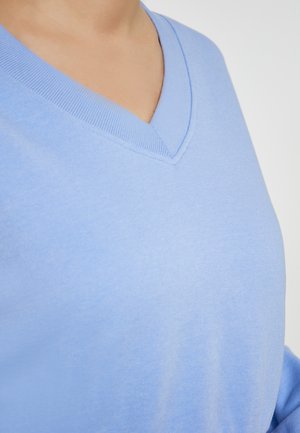 Pulover din bumbac de culoare albastru deschis, cu decolteu în V, textură moale și tiv cu dungi în jurul gulerului. Prim-plan care evidențiază netezimea țesăturii.