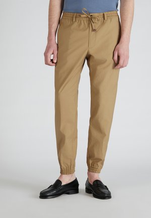 Beige, leichte Hose mit elastischem Bund und Kordelzug, mit gerafften Bündchen und glatter Textur. Getragen mit schwarzen Slippern.