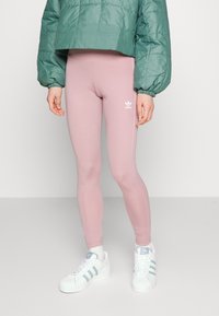 Rosa leggings i stretchmaterial, med en smal passform och en broderad vit adidas-logotyp på vänster höft, tillsammans med en grön pufferjacka.