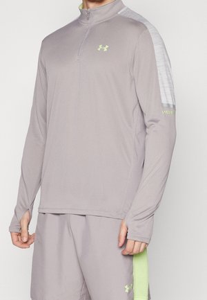 Mand iført lysegrå langærmet sportsbluse med kvart lynlås og matchende shorts med limegrønne Under Armour-logoer og detaljer.