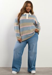 Maglione a righe in blu, beige e rosa con colletto bianco e bottoni, abbinato a jeans a gamba larga azzurri e sneakers bianche.