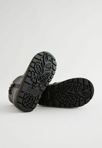 Schwarze Leder-Stiefeletten mit einem Reißverschluss, ausgestattet mit einer robusten, strukturierten Gummisohle mit Blattmustern. Langlebig und mit texturierter Oberfläche.