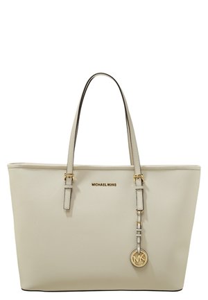 Sac cabas beige Michael Kors avec deux poignées, plaque logo dorée et pendentif circulaire MK suspendu sur un fond blanc uni.
