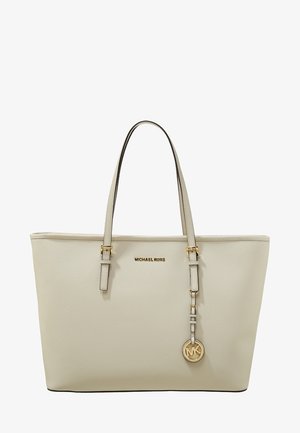 Beżowa torba typu tote marki Michael Kors z dwoma uchwytami, złotą plakietką z logo oraz wiszącym okrągłym zawieszonym znaczkiem MK na jednolitym białym tle.