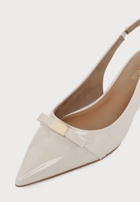 Λευκό γυαλιστερό επίπεδο παπούτσι slingback με μυτερή μύτη, μικρό διακοσμητικό φιόγκο και χρυσή ορθογώνια διακόσμηση στο μπροστινό μέρος.