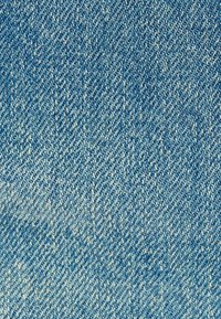 Denimkangas vaaleansinisessä sävyssä, jossa on tilkkutyökuvio, näyttää sileältä ja siinä on hienovaraista kulumista. Pienet valkoiset langat näkyvät kudoksessa.