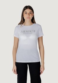T-shirt bianco in cotone con maniche corte e scollatura rotonda, con il logo argentato "ARMANI EXCHANGE" impreziosito sul davanti.