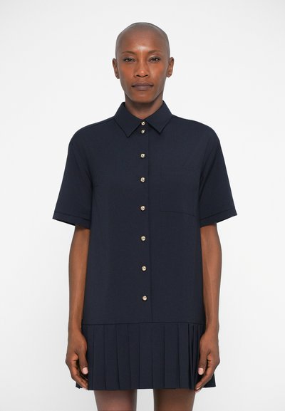Marineblauwe jurk met korte mouwen, een kraag, gouden knoopdetails en een geplooide zoom. Gemaakt van soepele stof met een getailleerde taille.