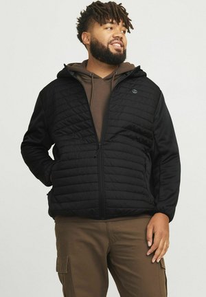 Black quilted jacket with a hood, front zipper, and two side pockets, worn over a brown hoodie. Features elastic cuffs and a logo on the chest.