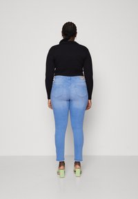 High-waisted light blue jeans with a smooth texture, two back pockets, and a tapered leg. Paired with a black long-sleeve top and green heels.