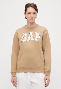 Sweatshirt castanho com letras brancas "GAP", adornado com bordados florais. Apresenta um decote redondo e punhos e bainha canelados.